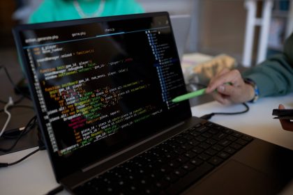 Focus on laptop screen with coded data and pen held by hand of young man.